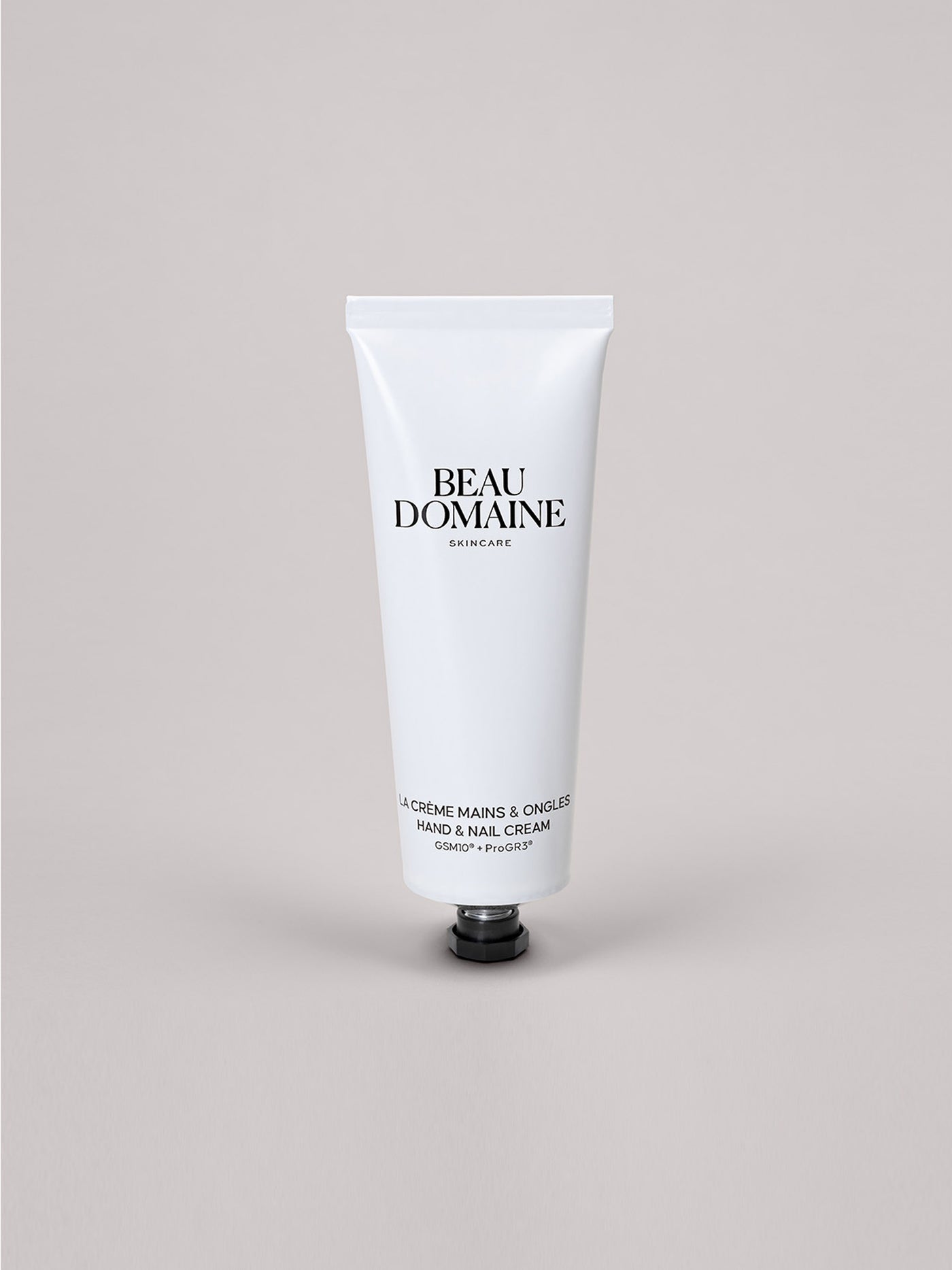 Weiße Tube Beau Domaine Hand- und Nagelcreme auf hellgrauem Hintergrund.