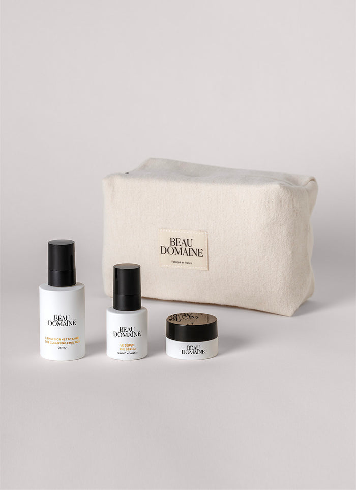 Kosmetik-Set mit Flaschen und einem Tiegel vor einem 'Beau Domaine' Beutel auf hellgrauem Hintergrund